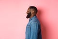 Profile of handsome bearded Black guy standing over pink background, smiling and looking left at copy space