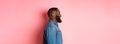 Profile of handsome bearded Black guy standing over pink background, smiling and looking left at copy space