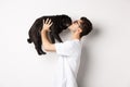 Profile of handsome young man kissing small cute dog face. Hipster guy loving his pug, standing over white background Royalty Free Stock Photo