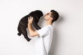 Profile of handsome young man kissing small cute dog face. Hipster guy loving his pug, standing over white background Royalty Free Stock Photo