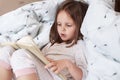 Profile of hard working curious smart girl learning to read, looking at text attentively, reading in voice, holding book, having Royalty Free Stock Photo