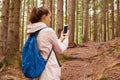 Profile of hiker woman wandering in forest, walking up slope, holding smartphone in both hands, switching it on, looking for