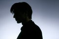 Profile portrait of a young man in black suit, poses in darkness, isolated on white background. Horizontal indoors shot. Royalty Free Stock Photo