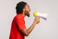 Profile of man with dreadlocks and beard wearing red casual style T-shirt, loudly screaming at megaphone, making protest, wants to