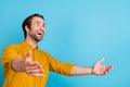 Profile photo of positive hopeful guy look empty space catch hands wear yellow shirt isolated blue color background