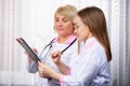 Profile photo of two medical workers discussing assignment sheet. Blond senior doctor, medical chief in white robe showing the