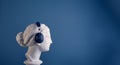 The profile of the plaster head of a graceful Aphrodite in huge blue audio headphones, against a blue background.