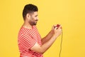 Profile portrait bearded man in red striped t-shirt holding in hands red gamepad joystick, grimacing playing video games