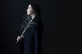 Profile portrait of beautiful brunette girl in coat, holding big dry plant leaf in studio, over black background. Royalty Free Stock Photo