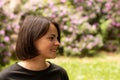 Profile portrait of a beautiful smiling woman in a black T-shirt against the background of a flowering bush Royalty Free Stock Photo