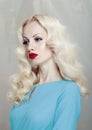 Profile portrait of a beautiful young blonde woman with curly hair and makeup, red lips, dressed in a blue dress. Royalty Free Stock Photo