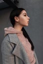 Profile portrait beautiful young brunette woman with long hair in pink stylish hoodie in fashionable coat near gray vintage wall. Royalty Free Stock Photo