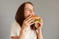 Profile portrait of Caucasian brown haired woman biting of appetizing delicious hamburger, being extremely hungry, enjoying junk Royalty Free Stock Photo