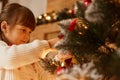 Profile portrait of Caucasian girl decorating Christmas tree, dressed white sweater, having dark hair, waiting new year eve, being Royalty Free Stock Photo