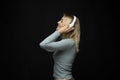 Profile portrait of charming blonde woman in massive white headphones listening to music on isolated black background. Royalty Free Stock Photo