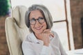 Profile portrait of cheerful elegant aged lady sitting chair beaming smile arm touch chin workstation indoors