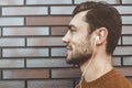 Profile portrait of a cheerful young man, listening to music in headset on mobile phone. Dressed in fashionable clothes. Outdoors Royalty Free Stock Photo