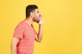 Profile portrait furious crazy man with beard in striped t-shirt loudly screaming holding hand near widely opened mouth