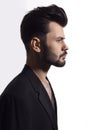 Profile portrait of a handsome, brutal bearded man posing in black suit, with naked torso, isolated white background. Royalty Free Stock Photo