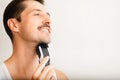 Profile portrait of handsome unshaven man shaving with modern electric razor indoors, copy space for text. Royalty Free Stock Photo