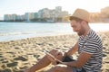 Happy man in hat sitting on beach using tablet Royalty Free Stock Photo