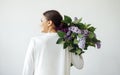 Profile portrait of a happy young woman in a white shirt holding a bouquet of lilacs on her shoulder