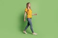 Profile portrait of nice positive lovely lady empty space walk wear yellow t-shirt jeans sneakers on green background