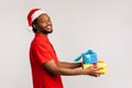 Profile portrait optimistic happy afro-american man with dreadlocks in santa claus hat holding gift boxes looking at camera with