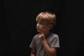 pensive handsome blonde little boy with finger near mouth on black background. Royalty Free Stock Photo