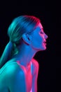 Profile portrait of sensitive and smiling young woman posing against black studio background in colorful neon light. Royalty Free Stock Photo