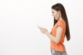 Profile portrait of shocked stunned expressive caucasian woman in orange t-shirt, holding smartphone and staring with