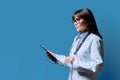 Profile portrait of female doctor holding clipboard on blue background, copy space Royalty Free Stock Photo