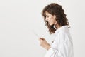 Profile portrait of stunning expressive young caucasian girl wearing wireless earbud and reading news in tablet, smiling