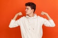 Profile portrait of teenager with stylish hairdo in fashionable hoodie demonstrating his arm muscles, strong and independent male