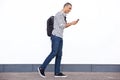 Profile portrait of young man walking and looking at cellphone by white wall Royalty Free Stock Photo