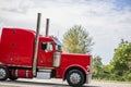 Profile of bright classic red big rig semi truck tractor with vertical chrome pipes running on the green highway Royalty Free Stock Photo