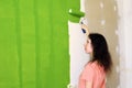 Profile of a pretty young woman in pink t-shirt is carefully painting green interior wall with roller in a new home and evaluating Royalty Free Stock Photo