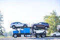 Profile of the running blue big rig classic car hauler semi truck transporting cars on the modular semi trailer