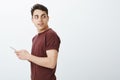 Profile shot of curious confident european male model in red t-shirt, holding smartphone and turning right to gaze at