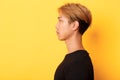 Profile shot of handsome stylish korean guy looking left with serious expression, standing over yellow background