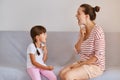 Profile shot of woman physiotherapist having lesson with small child girl for correct articulation, people sitting on sofa, small