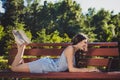 Profile side photo of cheerful positive lady lying bench outdoors in park typing email to friend studying online on