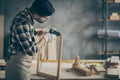 Profile side photo of serious concentrated worker man use electric hot glue gun to repair wooden construction frame work