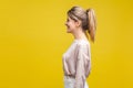 Profile side view of cheerful satisfied young woman with ponytale hairstyle and in casual beige blouse, isolated on yellow Royalty Free Stock Photo
