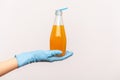 Profile side view closeup of human hand in blue surgical gloves holding bottle of orange drink