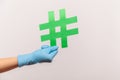 Profile side view closeup of human hand in blue surgical gloves holding green hashtag