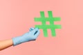 Profile side view closeup of human hand in blue surgical gloves holding green hashtag