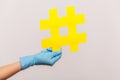 Profile side view closeup of human hand in blue surgical gloves holding yellow hashtag