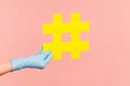 Profile side view closeup of human hand in blue surgical gloves holding yellow hashtag