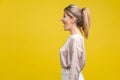 Profile side view of happy amazed blonde woman with ponytale hairstyle and in casual beige blouse, isolated on yellow background